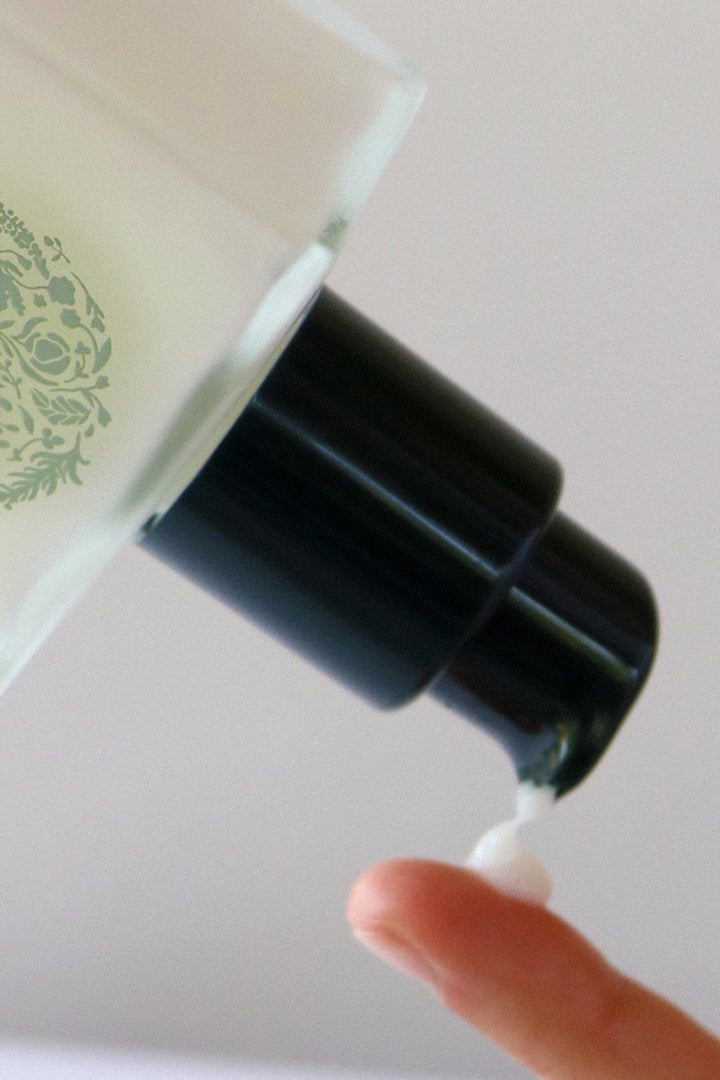 Close-up of a pump dispensing a drop of white leave-in conditioner.