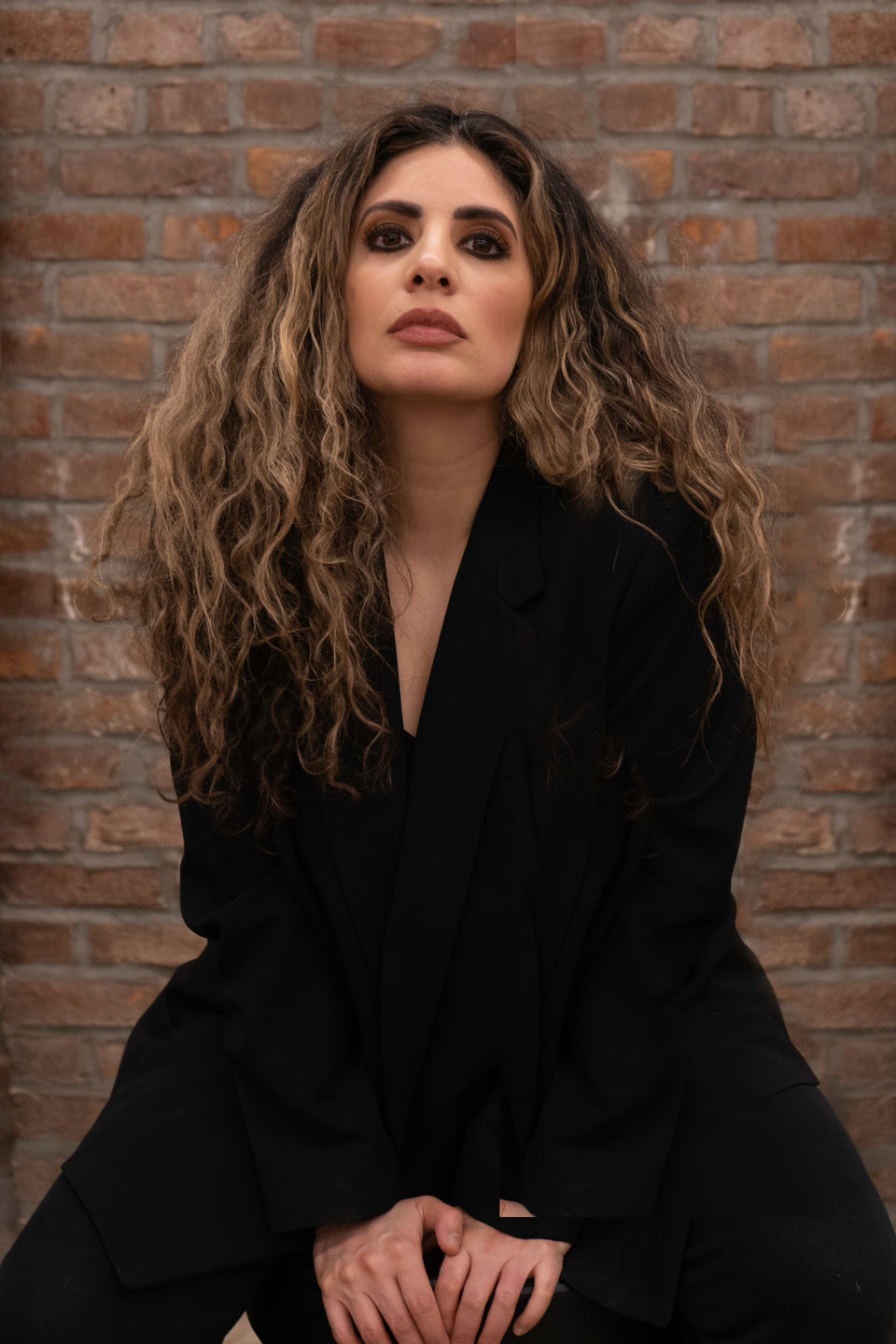 Portrait of Rachel Bodt, founder of Homecoming Salon, with long wavy brown hair against a brick wall.