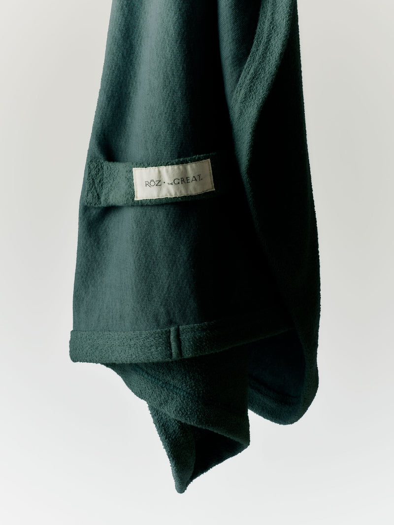 RŌZ + THE GREAT. Sweatshirt Hair Towel in Spruce, showing the dark green fabric and sewn label.